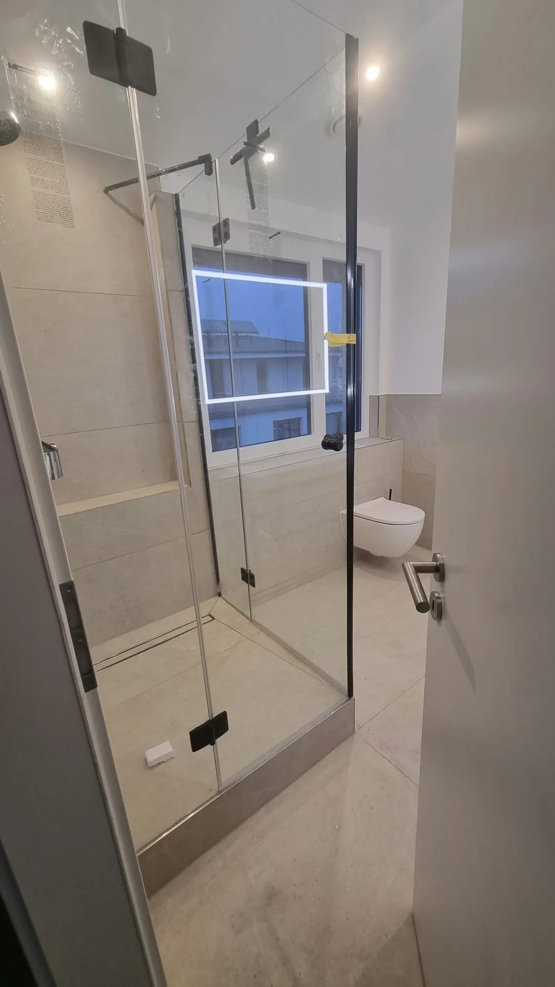 Bodengleiche Dusche mit schwarzem Rahmen in renoviertem Badezimmer mit Großflächenfliesen