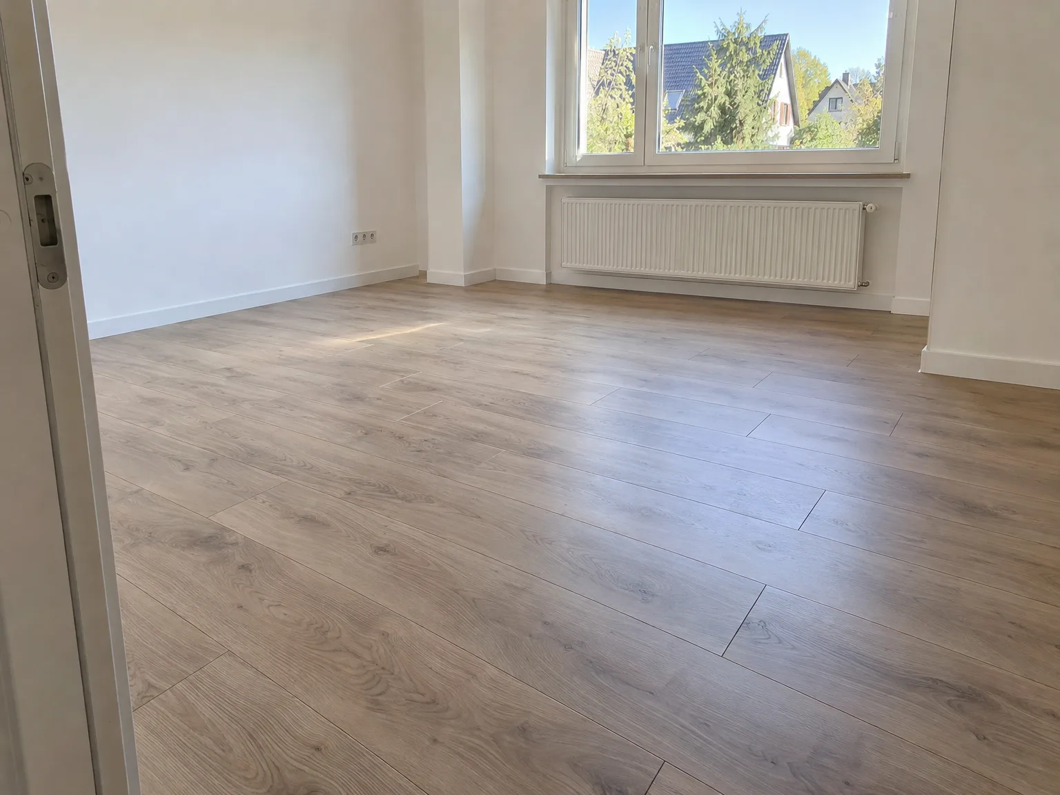 Neuer Laminatboden im hellen Zimmer mit weißen Wänden und großem Fenster