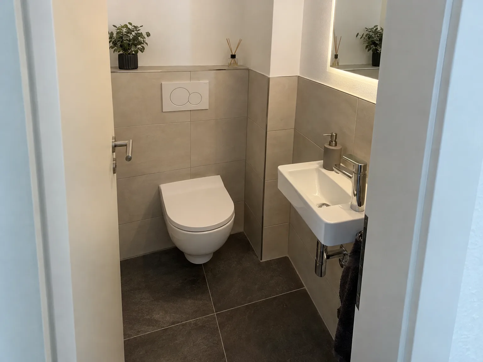 Saniertes Gäste-WC mit hängender Toilette, Handwaschbecken und grauem Fliesenbelag