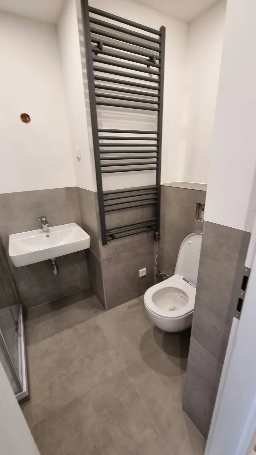 Modernes Gäste-WC mit grauen Wandfliesen, weißer Toilette, Wandwaschtisch und schwarzem Handtuchheizkörper